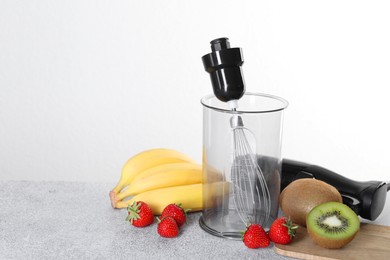 Photo of Hand blender kit, fresh fruits and strawberries on gray table against white background, space for text