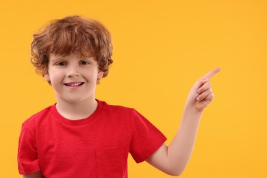 Photo of Portrait of cute little boy pointing at something on orange background