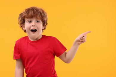 Photo of Portrait of emotional little boy pointing at something on orange background