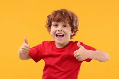 Photo of Portrait of happy little boy showing thumbs up on orange background