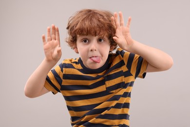 Photo of Portrait of emotional little boy showing tongue on grey background