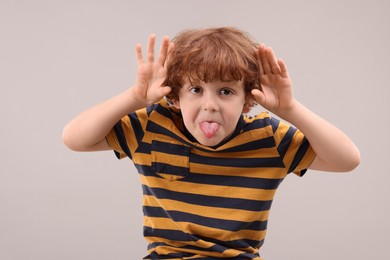 Photo of Portrait of emotional little boy showing tongue on grey background