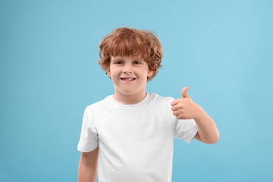 Photo of Portrait of cute little boy showing thumbs up on light blue background