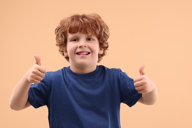 Photo of Portrait of cute little boy showing thumbs up on beige background