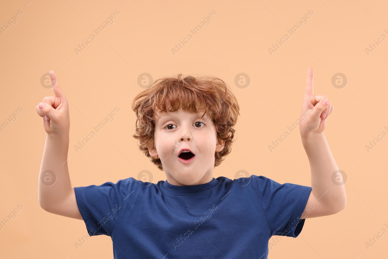 Photo of Portrait of emotional little boy pointing at something on beige background