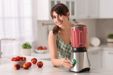 Photo of Young woman making delicious smoothie with blender at white marble table in kitchen