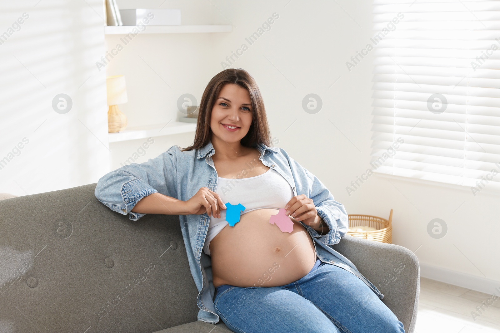 Photo of Beautiful pregnant woman with paper hearts on sofa at home. Expecting twins