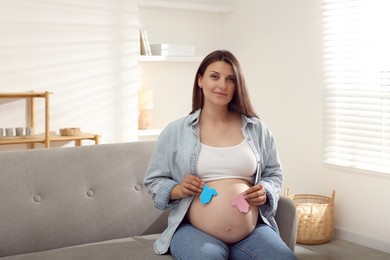 Photo of Beautiful pregnant woman with paper hearts on sofa at home. Expecting twins