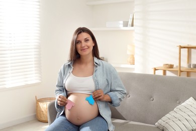 Photo of Beautiful pregnant woman with paper hearts on sofa at home. Expecting twins