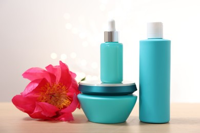 Photo of Set of hair care cosmetic products and peony flower on wooden table against light background with blurred lights