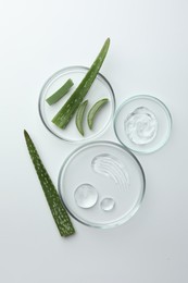 Photo of Petri dishes with different cosmetic products and aloe vera leaves on white background, flat lay