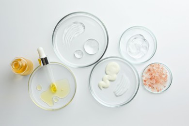 Photo of Petri dishes with different cosmetic products on white background, flat lay