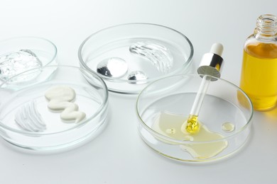 Petri dishes with different cosmetic products on white background, closeup