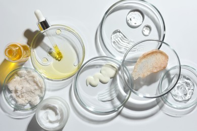 Petri dishes with different cosmetic products on white background, flat lay