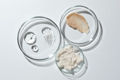 Photo of Petri dishes with different cosmetic products on white background, flat lay