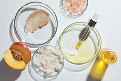 Petri dishes with different cosmetic products and peach on white background, flat lay