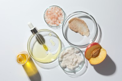 Petri dishes with different cosmetic products and peach on white background, flat lay