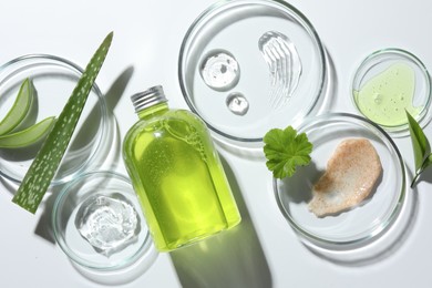 Petri dishes with different cosmetic products and aloe vera leaves on white background, flat lay