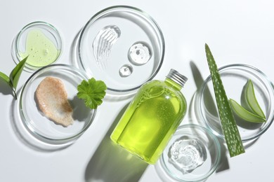 Photo of Petri dishes with different cosmetic products and aloe vera leaves on white background, flat lay