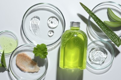 Petri dishes with different cosmetic products and aloe vera leaves on white background, flat lay