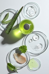 Photo of Petri dishes with different cosmetic products and aloe vera leaves on white background, flat lay