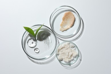 Petri dishes with different cosmetic products and leaves on white background, flat lay