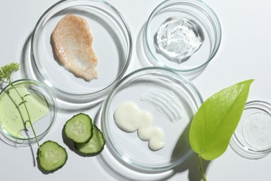 Photo of Petri dishes with different cosmetic products and leaves on white background, flat lay