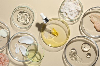 Photo of Petri dishes with different cosmetic products on beige background, flat lay