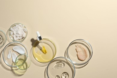 Photo of Petri dishes with different cosmetic products on beige background, flat lay. Space for text