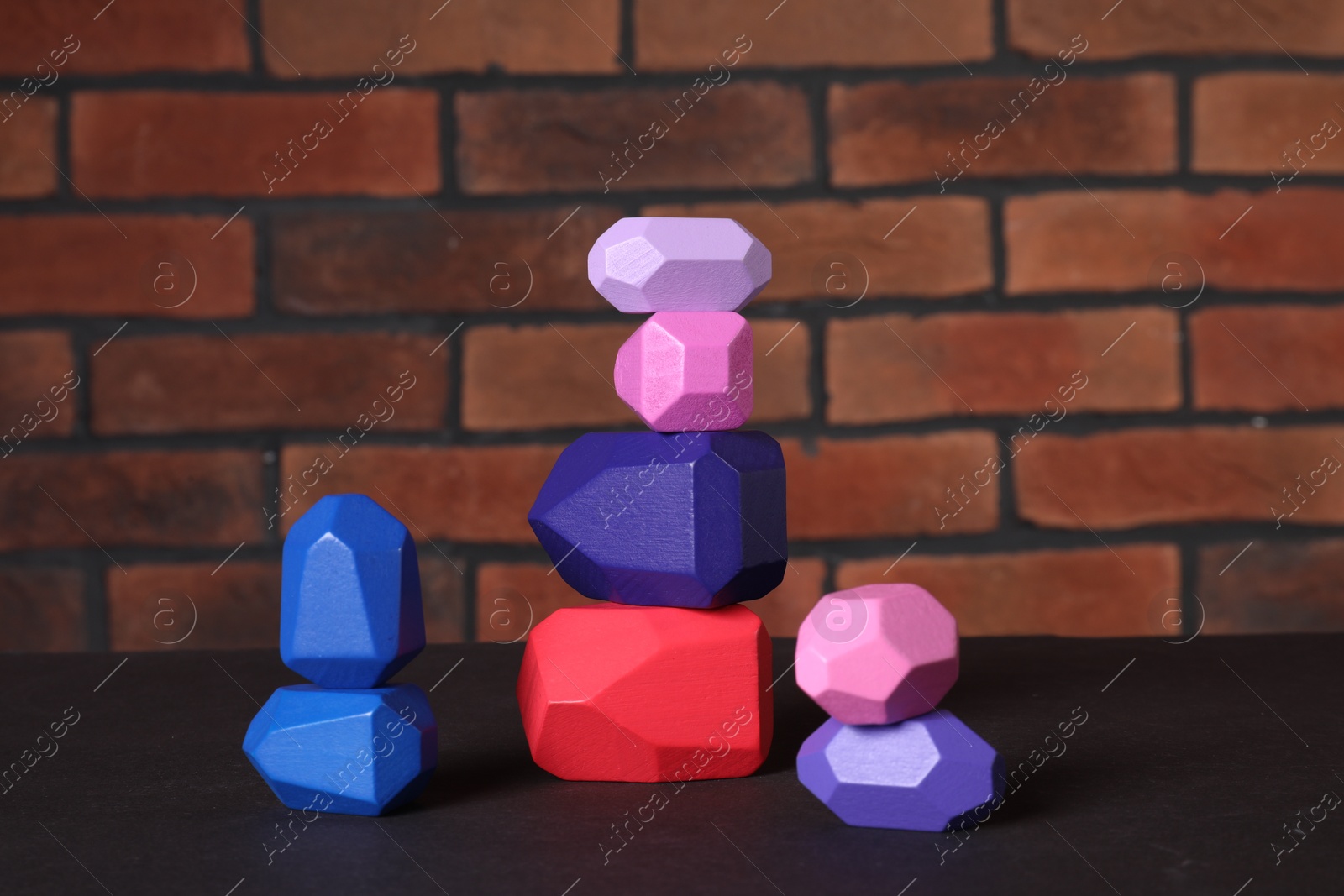 Photo of Many colorful balancing stones on brown table against brick wall