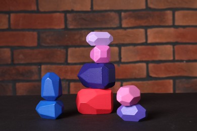 Photo of Many colorful balancing stones on brown table against brick wall