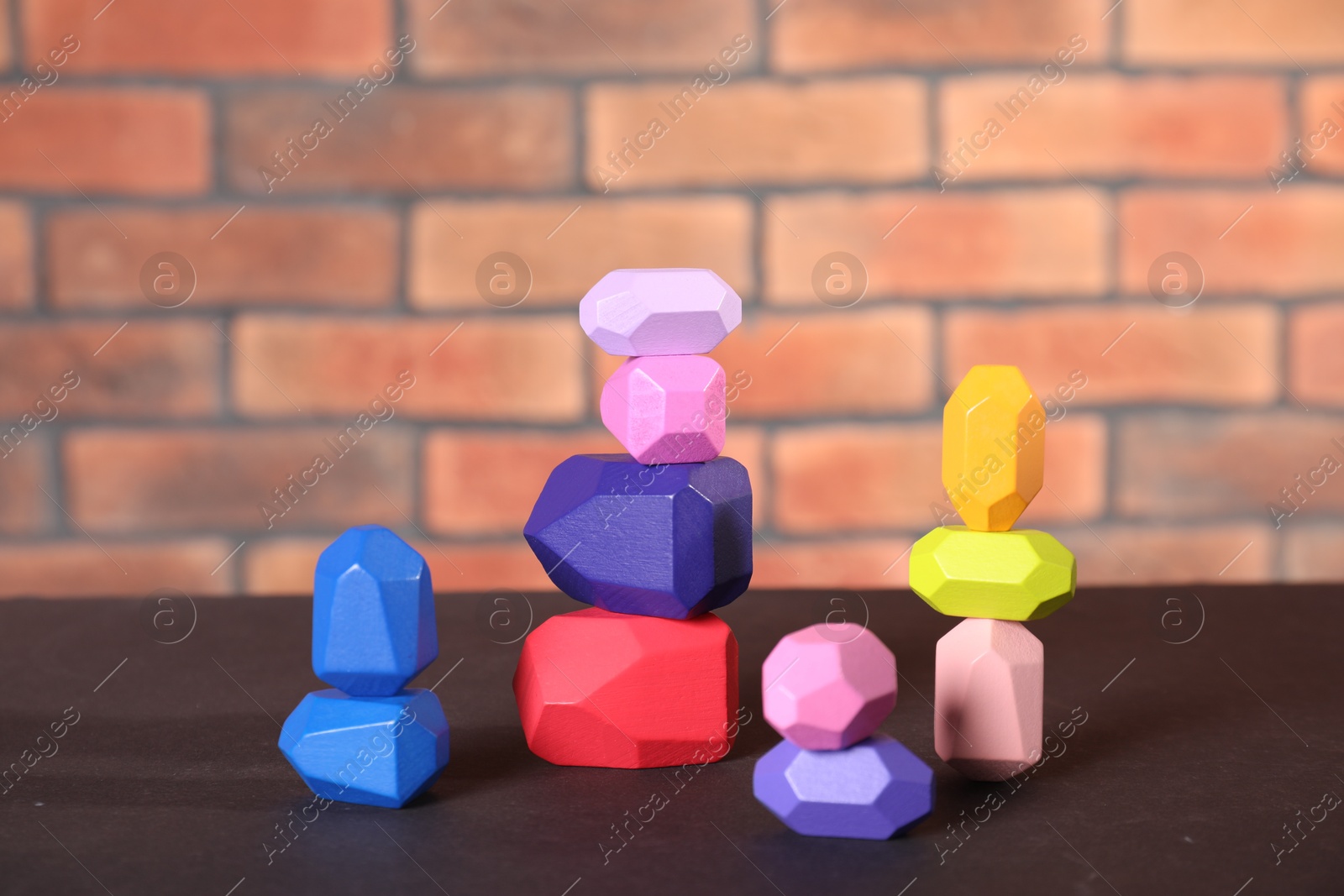 Photo of Many colorful balancing stones on brown table against brick wall