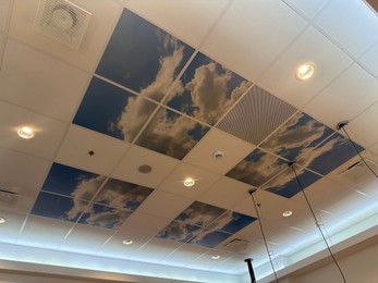 White ceiling with lighting and pictures of blue sky indoors, low angle view