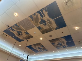 White ceiling with lighting and pictures of blue sky indoors, low angle view