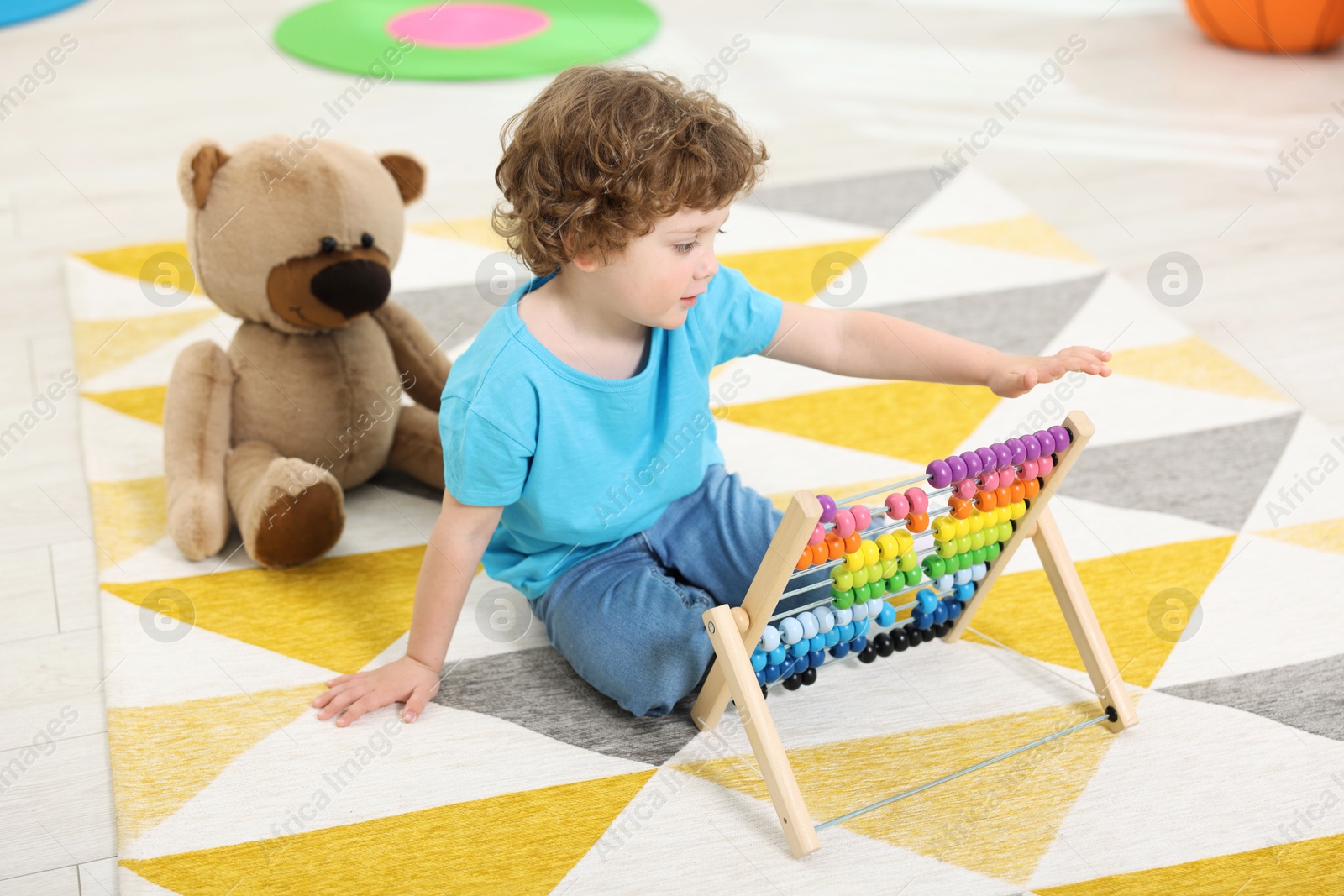 Photo of Cute little boy playing with wooden abacus on floor in kindergarten