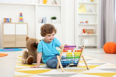 Cute little boy playing with wooden abacus on floor in kindergarten