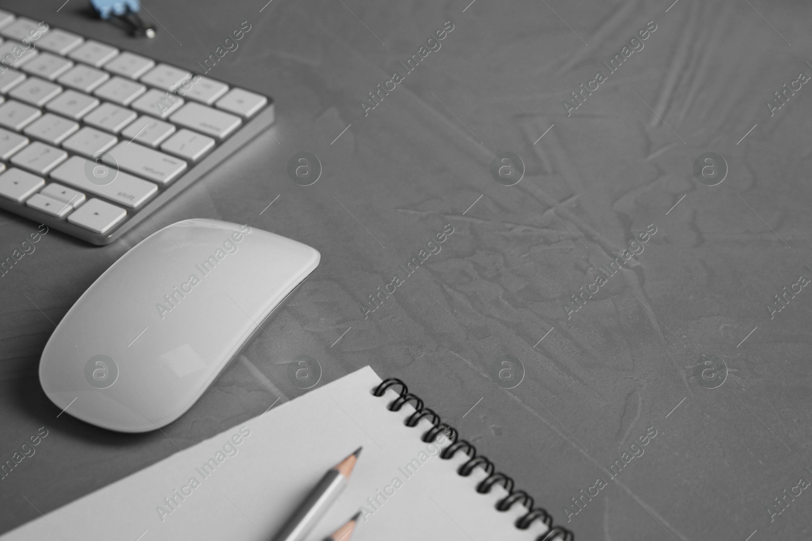 Photo of Wireless mouse, notebook, pencils and computer keyboard on grey textured table, closeup. Space for text