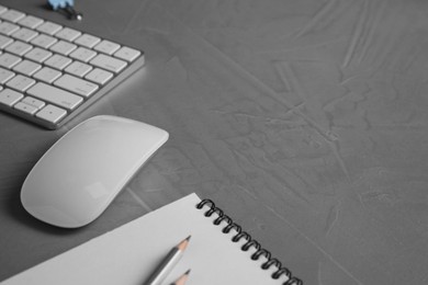 Wireless mouse, notebook, pencils and computer keyboard on grey textured table, closeup. Space for text