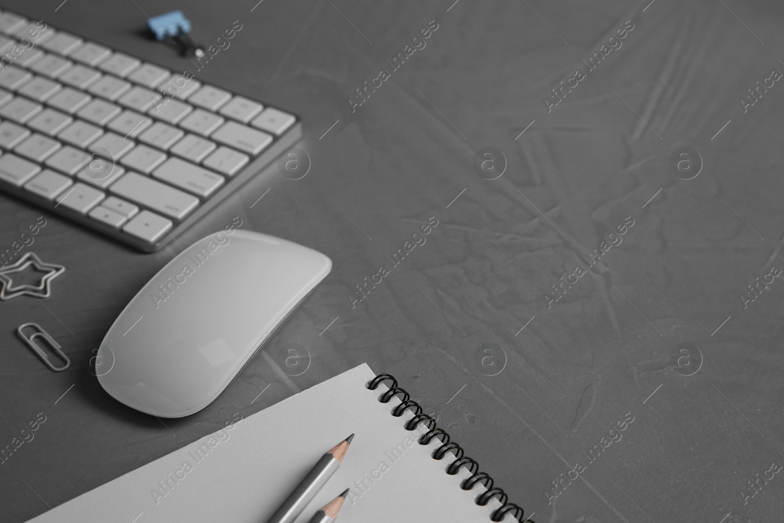 Photo of Wireless mouse, notebook, pencils and computer keyboard on grey textured table, closeup. Space for text