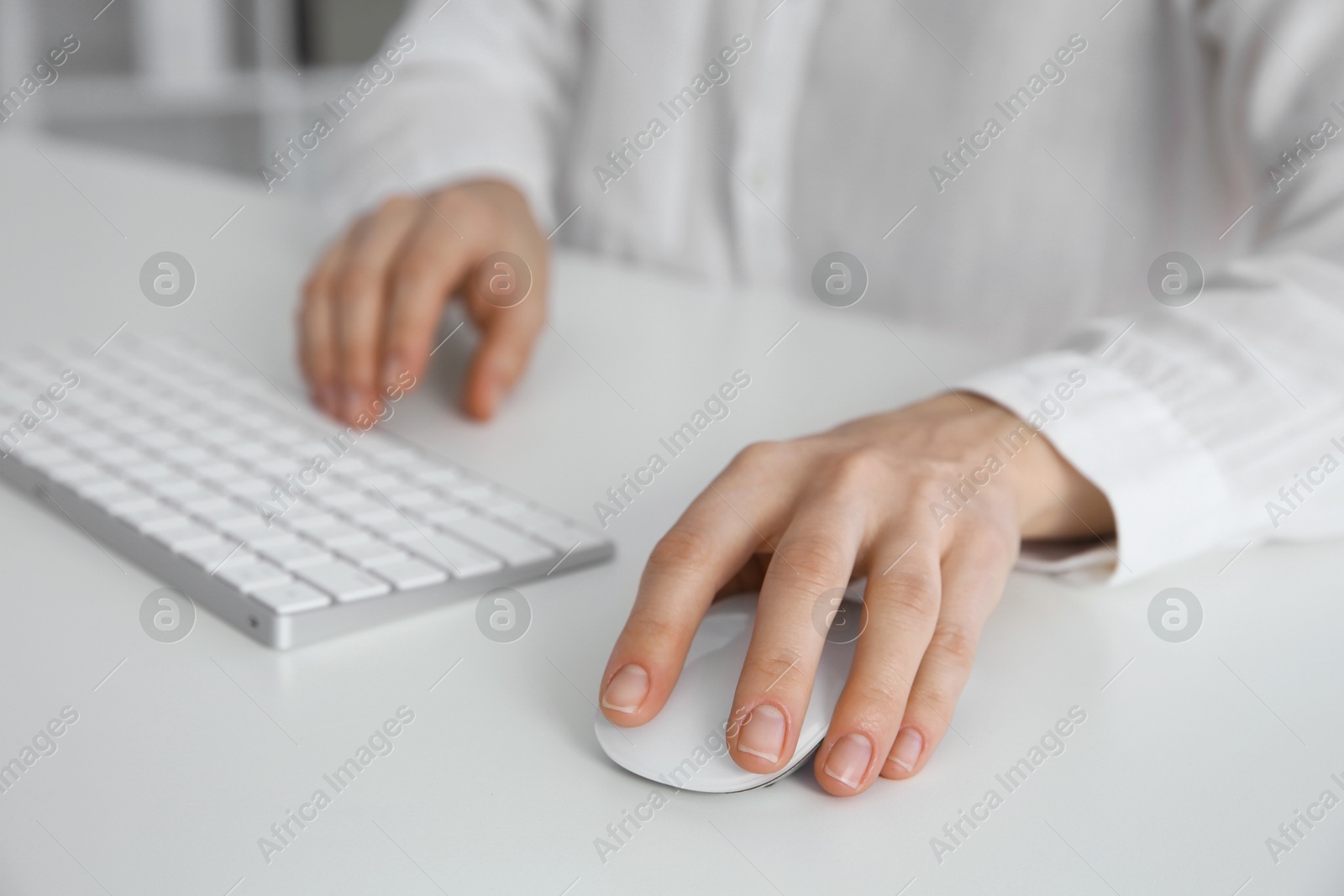 Photo of Woman working with wireless mouse and computer keyboard at white table indoors, closeup