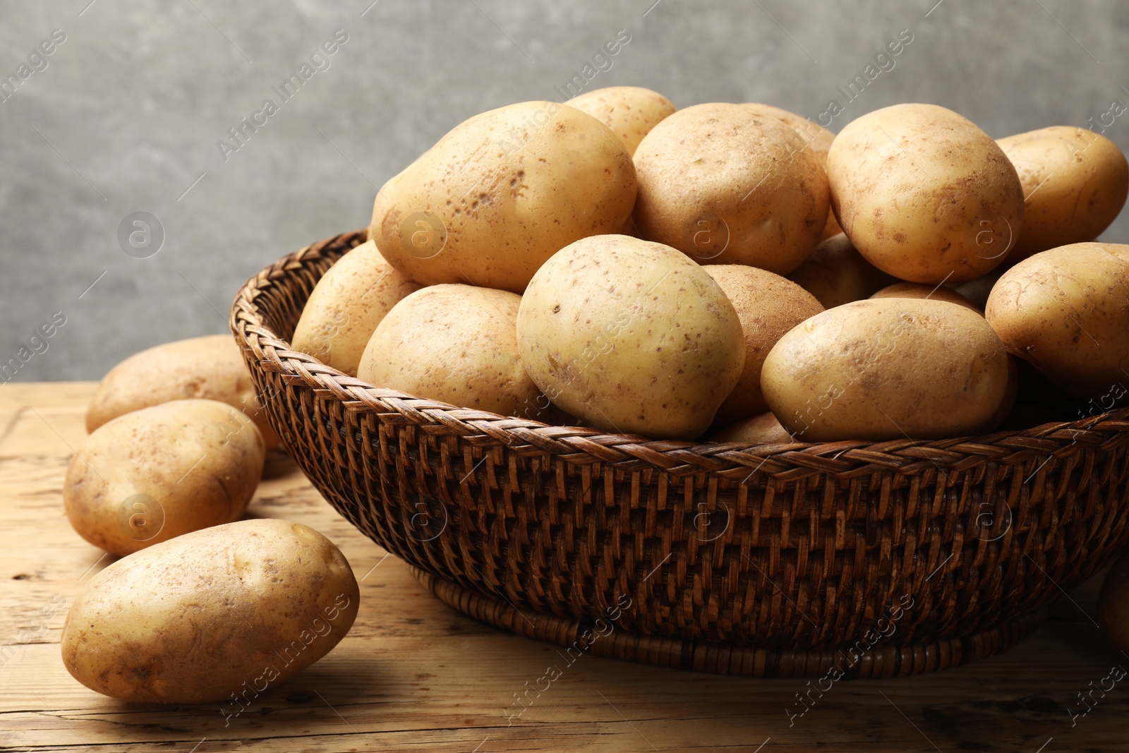 Photo of Many fresh potatoes in wicker basket on wooden table, closeup