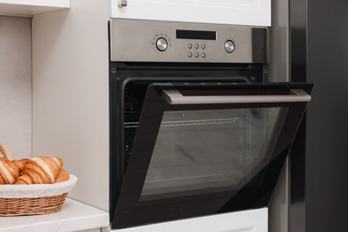 Photo of Open electric oven and croissants in kitchen. Cooking appliance