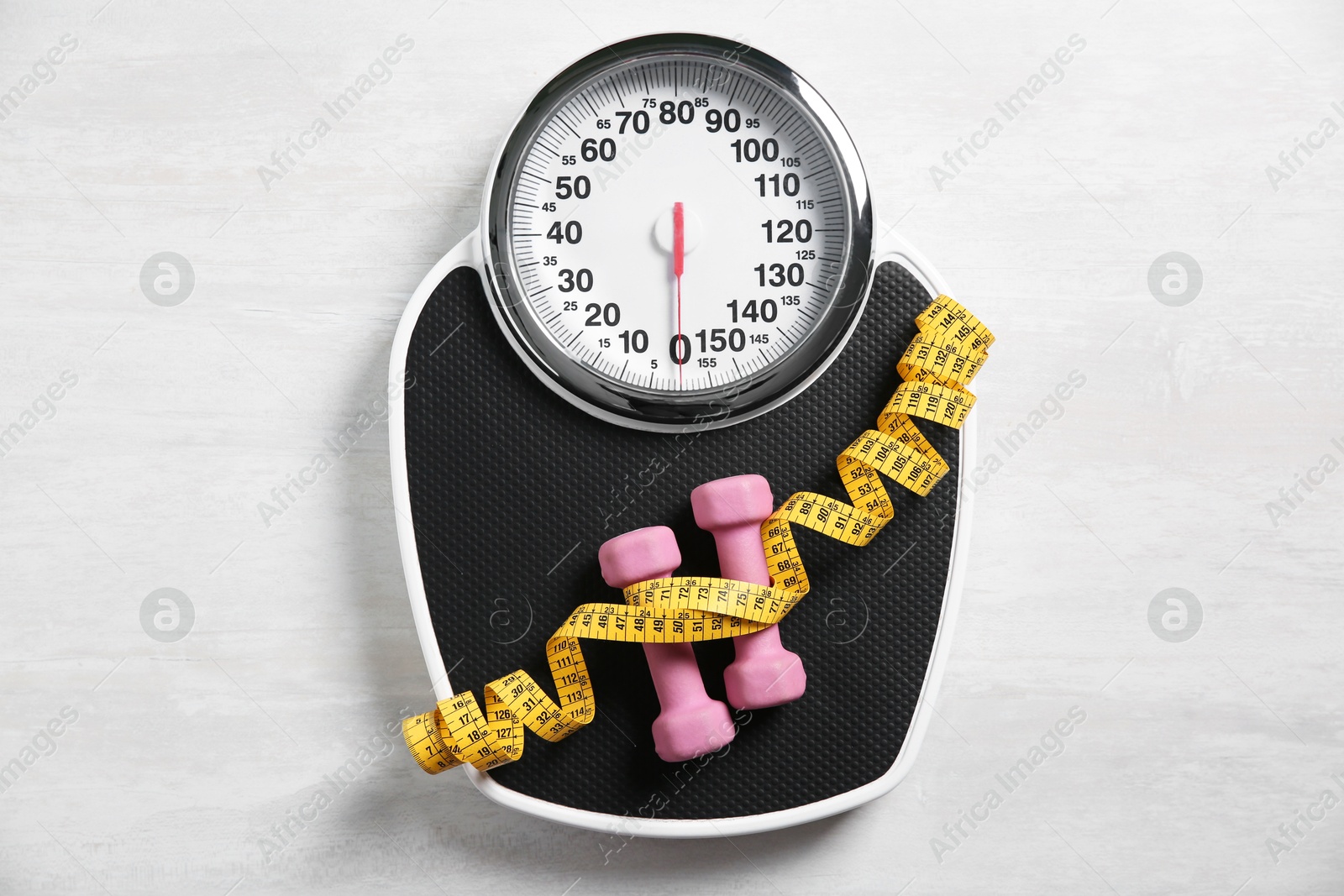 Photo of Bathroom scale, measuring tape and dumbbells on white wooden background, flat lay