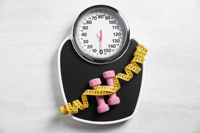 Photo of Bathroom scale, measuring tape and dumbbells on white wooden background, flat lay