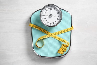 Photo of Scale tied with measuring tape on light wooden background, top view