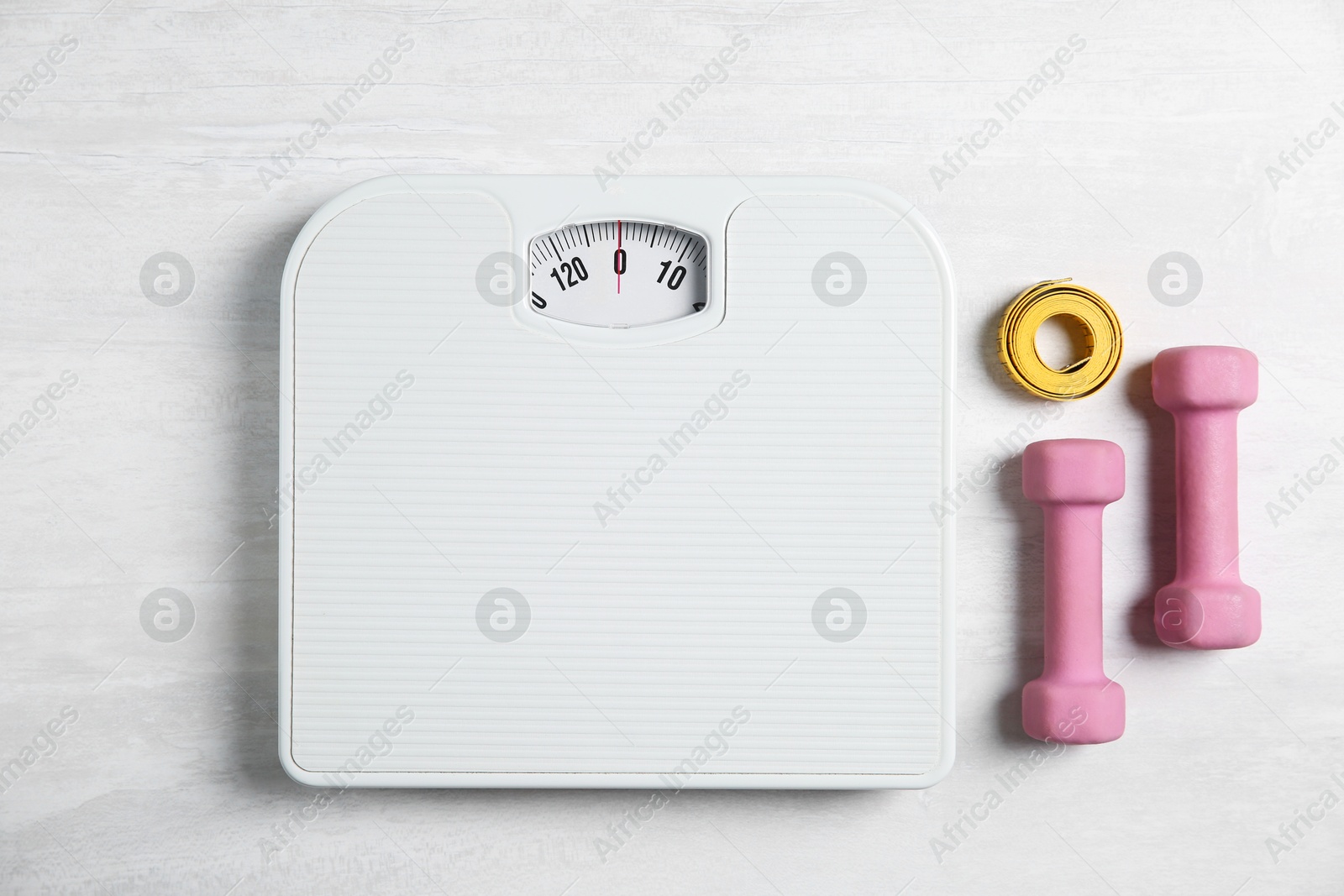 Photo of Bathroom scale, measuring tape and dumbbells on white wooden background, flat lay