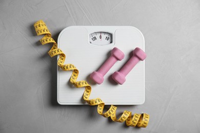 Photo of Bathroom scale, measuring tape and dumbbells on grey textured background, flat lay