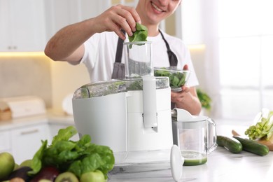 Man putting fresh basil into juicer at white marble table in kitchen, closeup