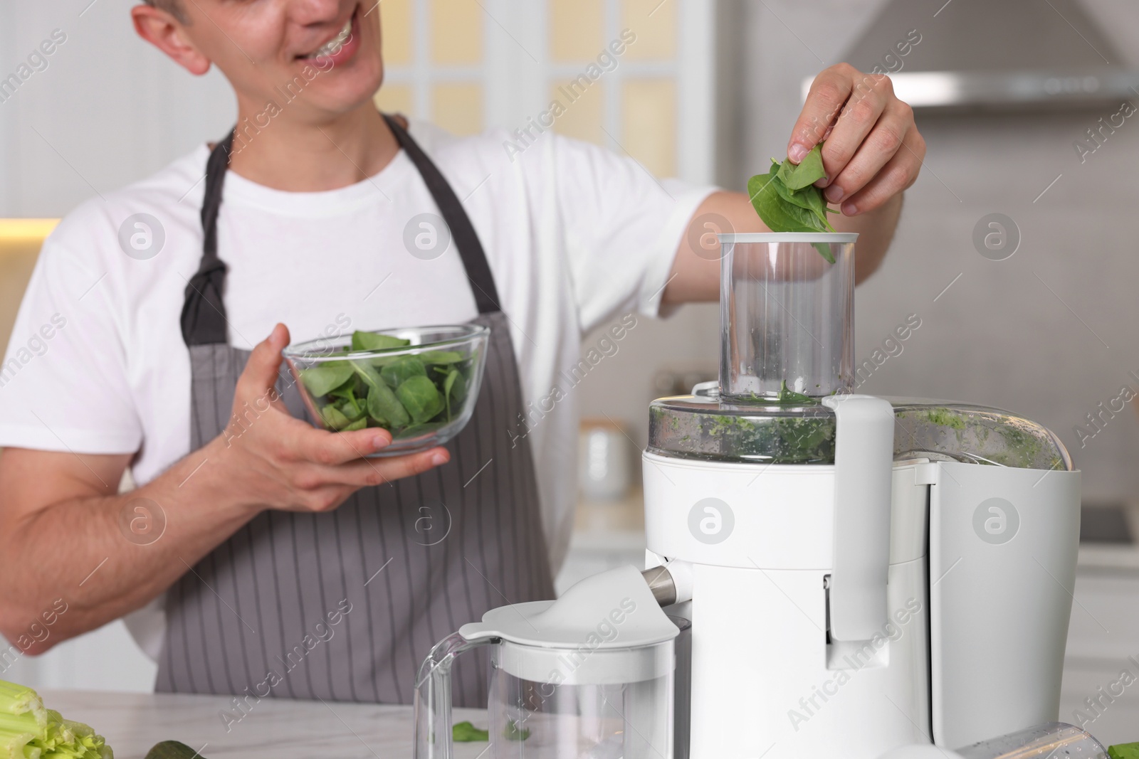 Photo of Man putting fresh basil into juicer in kitchen, closeup