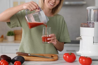 Photo of Woman pouring tomato juice into glass in kitchen, closeup. Juicer and fresh products on white marble table